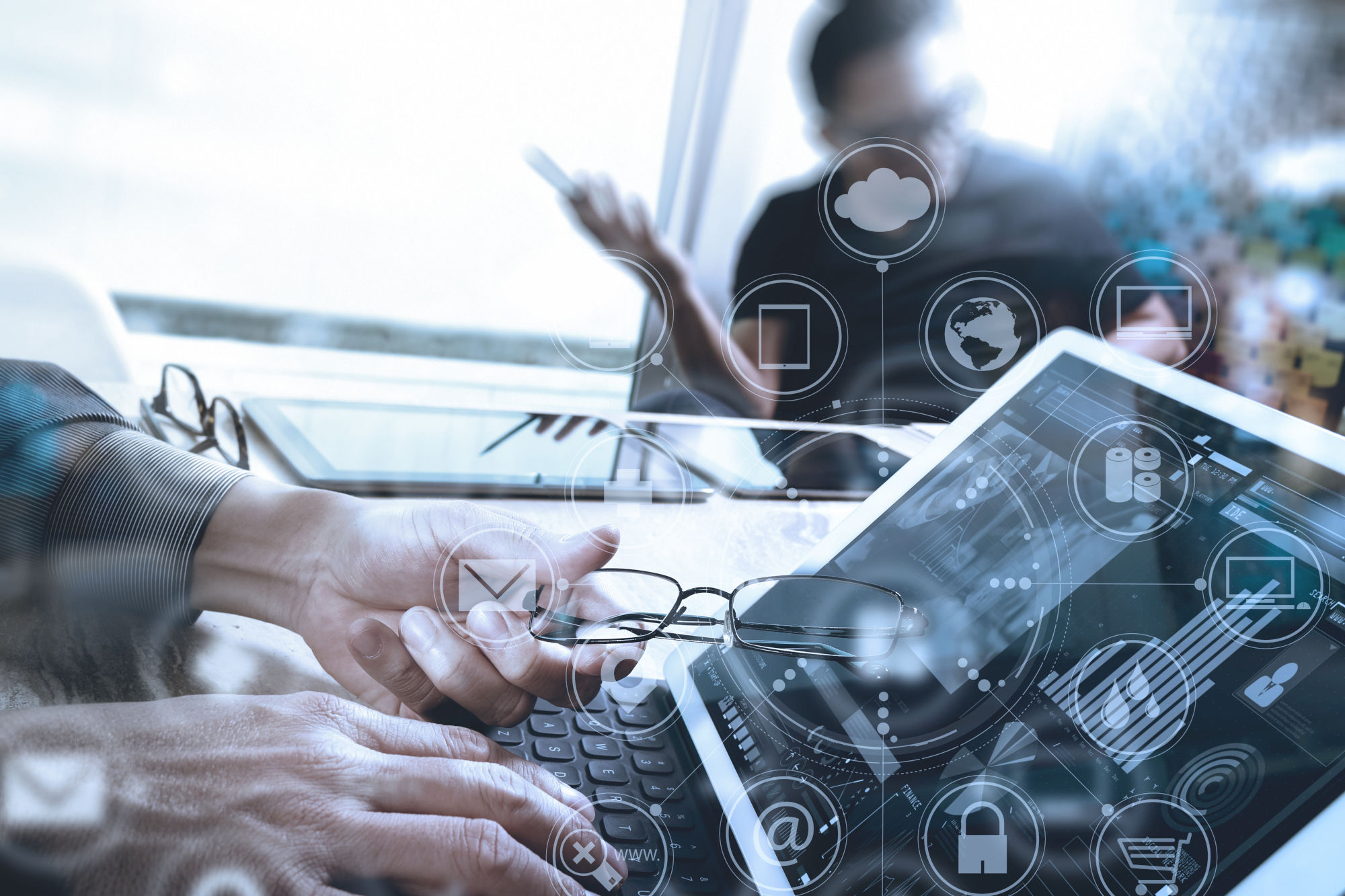 Man holding folded glasses while using a laptop, with icons overlaid in front