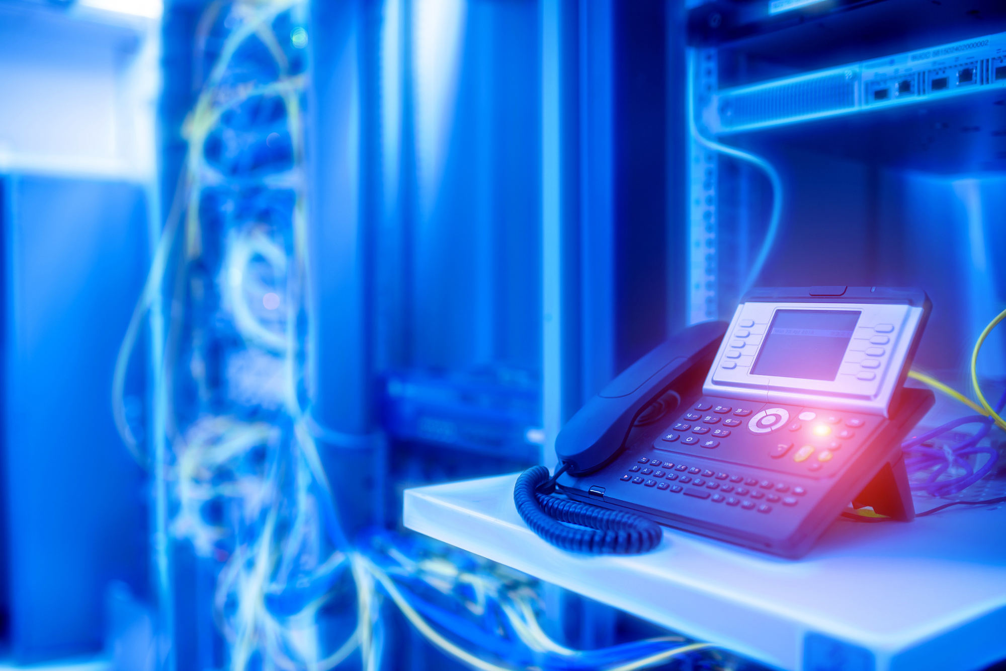 VoIP phone with a lit, red button in a blue-tinged server room